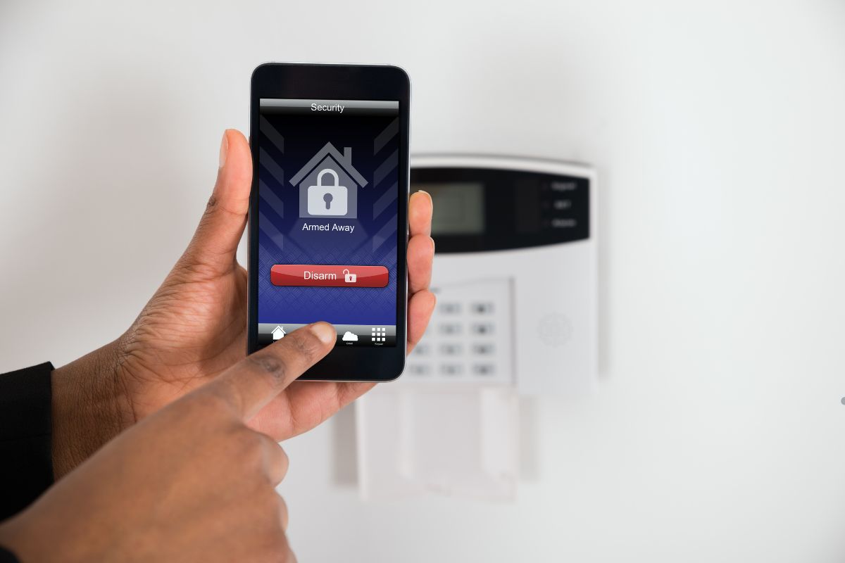  A person using a smartphone to manage various types of home security alarm systems.