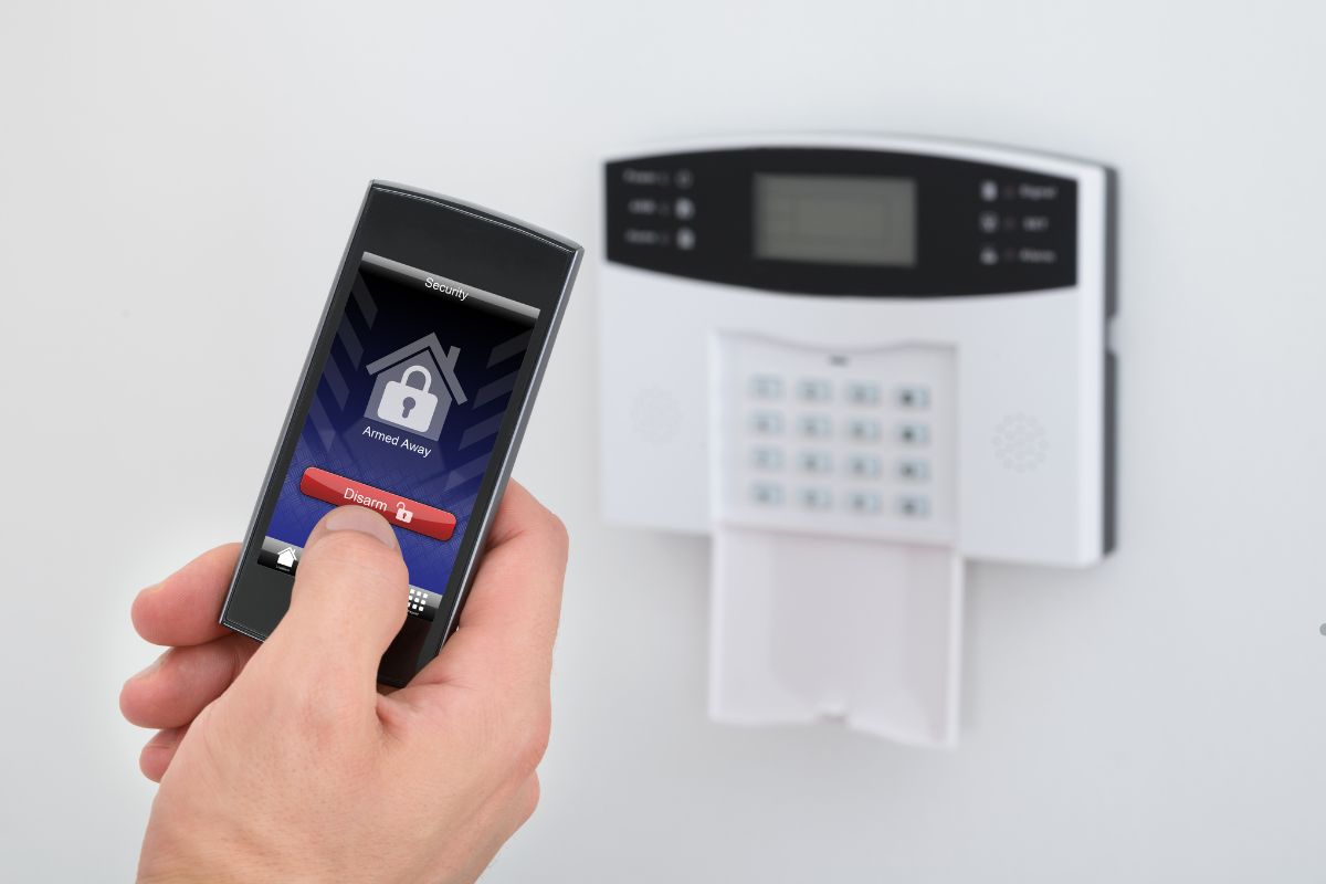  A person using a cell phone to control a home alarm system, emphasizing the importance of securing the home's perimeter.